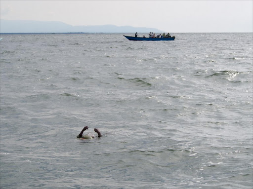 Uganda Police divers and local fishermen sail past the body of a Congolese refugee floating during their search for victims of a boat disaster on Lake Albert.