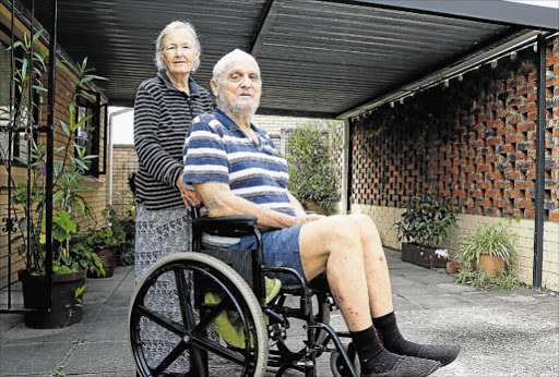 ON THE LOOKOUT: Rodney Hodgkinson in his borrowed wheelchair while the search for his red wheelchair continues at Frere hospital. His wife Mary stands next to him Picture: NONSINDISO QWBE