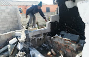 A neighbour examines the remains of the Khayelitsha house burned down by neighbours on September 3 2019.