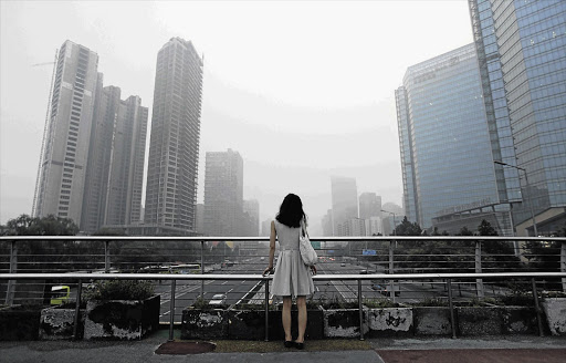 A woman stands on an overhead bridge on a typically hazy day in Beijing's central business district.