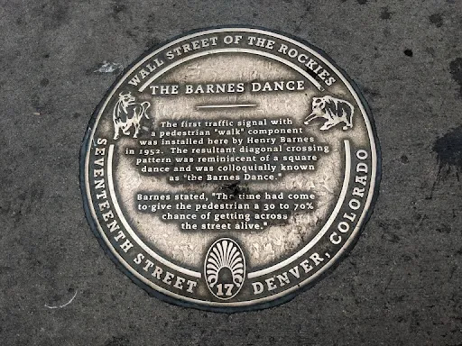 Sidewalk plaque marking the creation by traffic engineer Henry Barnes of the first traffic lights that included a pedestrian “Walk” signal. The arrangement triggered diagonal crossings that...