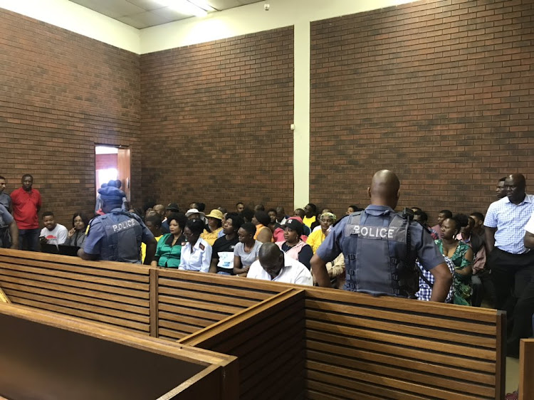 Police officers keep watch over members of the public at the Lenasia Magistrate’s Court, where a 61-year-old man faces seven charges of murder, following the killing of a family in Vlakfontein, south of Johannesburg.