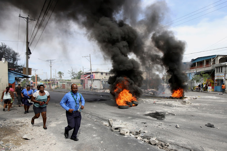 People walk past a burning street barricade during a demonstration against fuel shortages, in Port-au-Prince, Haiti on October 23, 2021.
