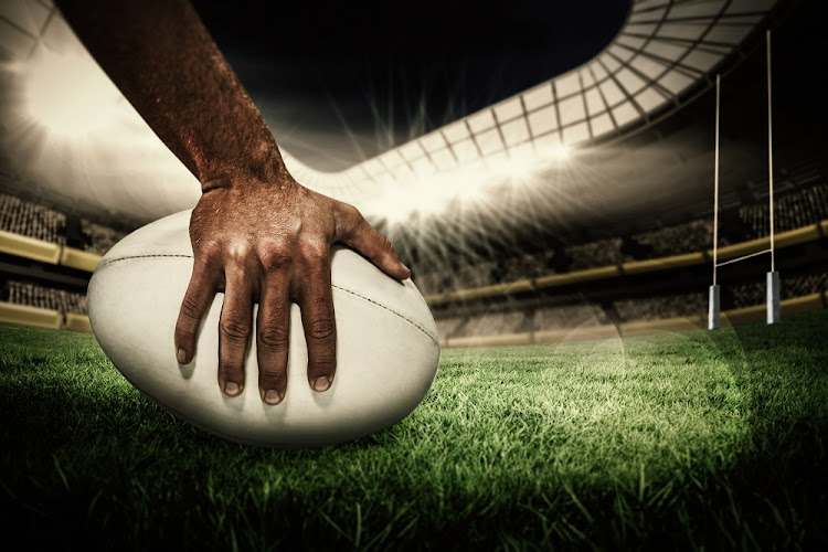 Close-up of sports player holding ball against rugby pitch