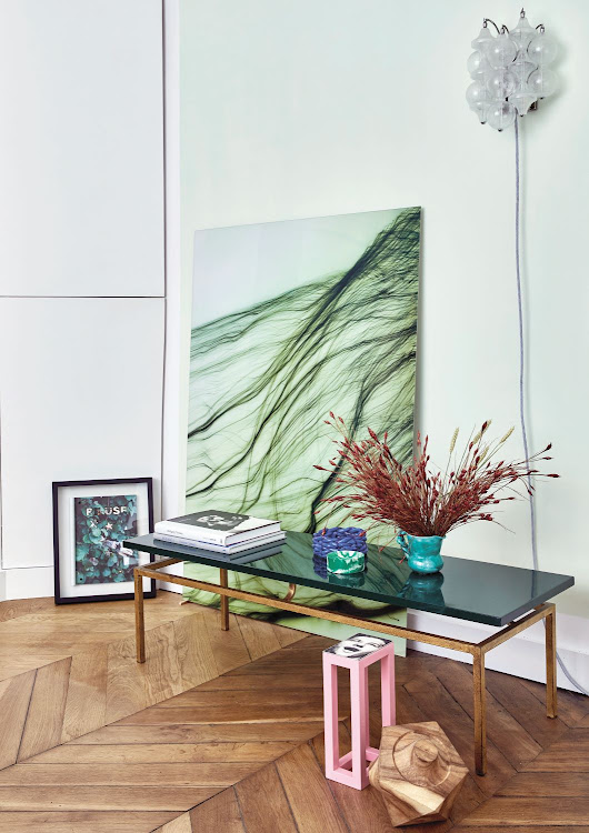 In the main bedroom, a vintage 1950s brass table from a Paris flea market displays various artworks and collectibles. The small artwork is by French artist Marc Turlan, while the ceramics were found at local and Italian markets. On the floor is a pink art piece by Aumas. The geometric wooden sculpture was brought back from a trip to Africa.