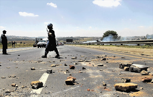 OBSTACLE COURSE: A police officer clears Randfontein Road outside Roodepoort, western Johannesburg, yesterday after protesters from the Vlakfontein informal settlement forced its closure by setting up barricades and burning tyres.