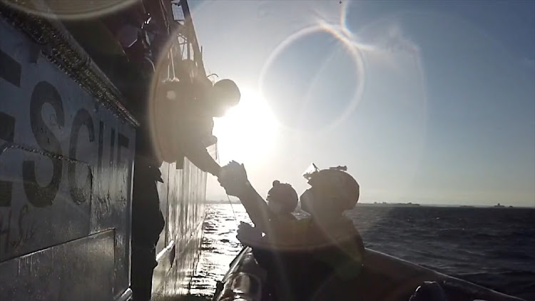 A still image taken from a video shows a rescuer of Spanish NGO Open Arms helping a migrant boarding a dinghy in the Mediterranean Sea, November 14, 2020. Two women and one man were confirmed dead on arrival at the Tenerife port on Friday.