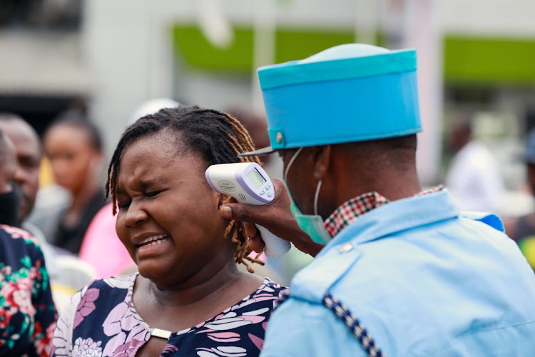 A security guard uses a thermal scanner to check a woman's temperature as she enters the Tejuoso shopping complex at the Yaba market. Nigerian health workers demanding a hazard allowance for treating coronavirus patients have called off their strike.