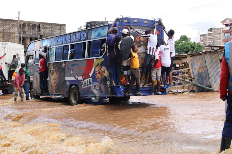 Residents holds on a mini bus to cross a flooded road at a bridge connecting Mwiki and Kasarani on April 24, 2024.