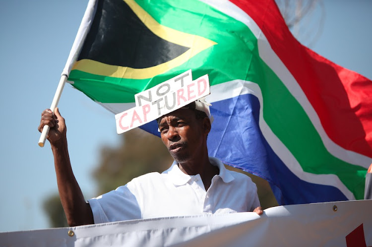 Ali Gule from NPO, Organisation Undoing Tax Abuse (Outa) holds a flag during a picket, 20 August 2018, outside the State Capture Inquiry in Parktown, Johannesburg.