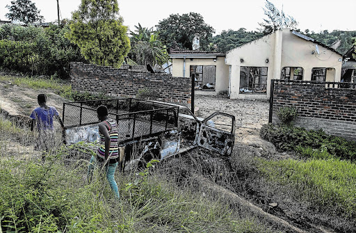 VIGILANTE JUSTICE: Residents of Kubjana village in the Tzaneen district walk past the burnt-out car and house of a shopkeeper