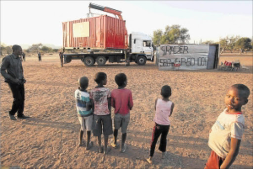 RELIEF EFFORT: Children watch as a container, sponsored as a mobile office by Vodacom, is offloaded at Selowe Primary School in Silvermine in Limpopo, where classes have been held under trees. PHOTO: KEVIN SUTHERLAND