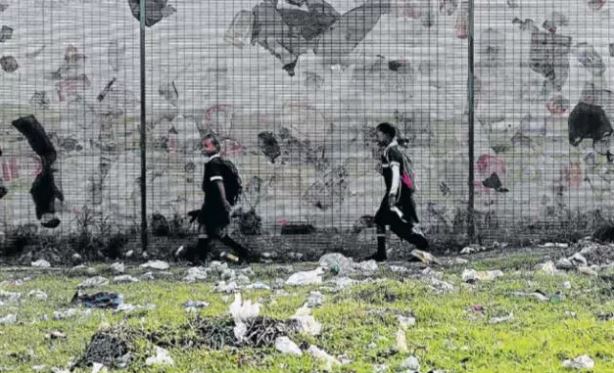 Lee-Ann Johnson, 9, and Anam Masatie, 8, from Sedeberg Primary School in Booysen Park walk past a fence as the wind blows plastic bag refuse against it. (File photo)