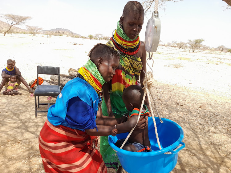 Jessica Chegem a Community Health Volunteer of Natuntun, Loima Sub County putting a child on a trough to measure the weight of a child on weighing scale
