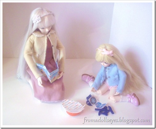 Two ball jointed dolls assembling a Kinder Joy toy.  The larger doll is trying to read the instructions and the smaller younger doll is putting the toy together with no effort at all.