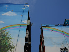 two buildings with a painted rainbow, blue sky, and birds with a real blue sky in the background