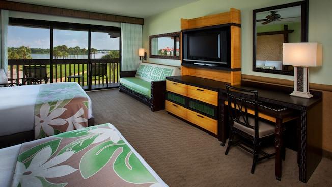 A desk, TV-dresser, daybed across from 2 queen beds and, beyond, a balcony and Seven Seas Lagoon