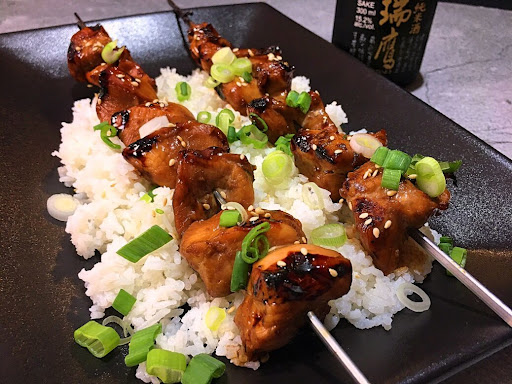 A couple delicious Yakitori Chicken Skewers sitting on a bed of rice and garnished with chopped green onions. 