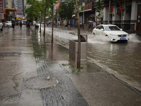 water coming out of a sewer hole on a sidewalk next to a flooded street in Taiyuan, China