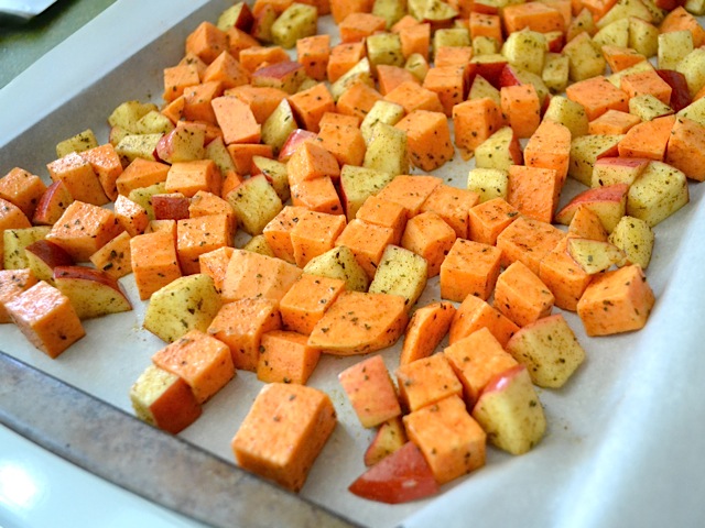 Sweet potato and apples spread out on baking sheet lined with parchment paper 