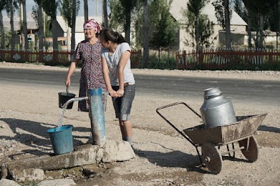 An einer Pumpe neben der Dorfstraße versorgt sich eine Frau mit Wasser