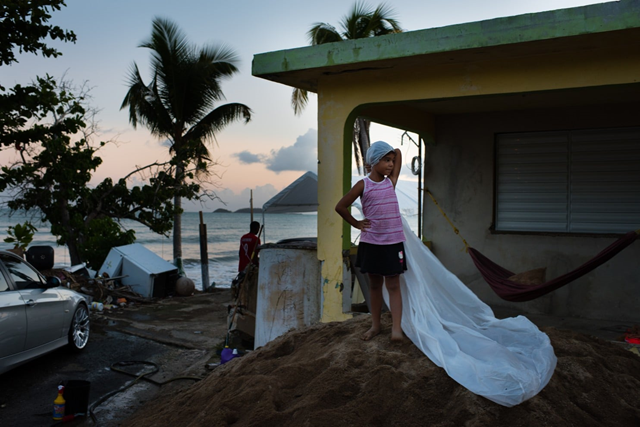 In the Puerto Rico barrio known as “La Ola” — the wave — Damarys Cantero’s 6-year-old daughter, Sharmelehia, pretends that a piece of plastic, which once covered a pile of construction sand, is a bridal veil while playing in front of her cousin’s house. Their house was wrecked by Hurricane Maria, and one year later, still has not been fully rebuilt. Photo: Sarah L. Voisin