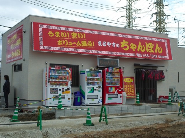 まるやす食堂の外観。店頭の赤い看板には、うまい！安い！ボリューム満点！と書かれてる。