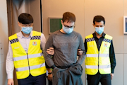 Police officers escort Canadian David James Roach in Singapore, March 2020, in this handout photo released to Reuters on July 8, 2021. 