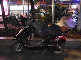 man sleeping on a motorbike with his legs propped up on the handlebars