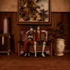 Zuko and Mai sitting together, next to a vase, a painting behind them. His arm is around her.