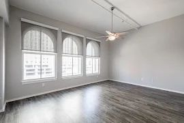 Spacious living room with wood inspired floors, high ceilings, a ceiling fan, and 3 large windows with arches