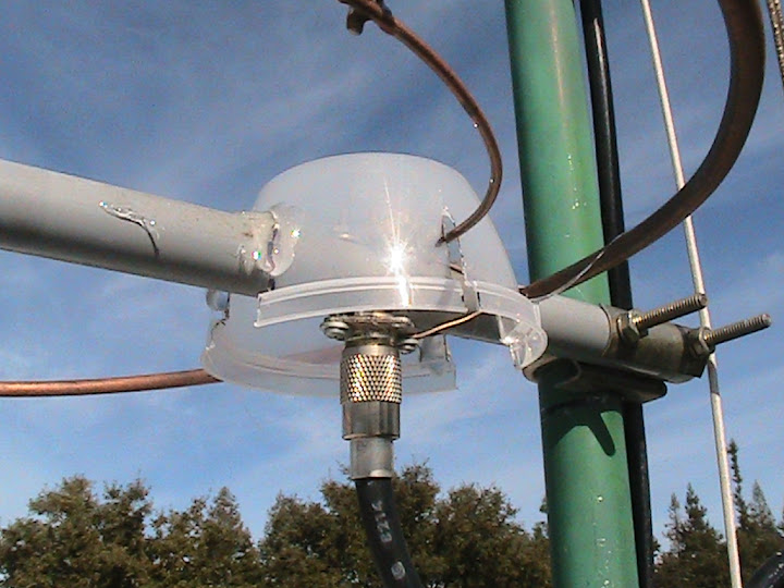 A
                      weather shield was fashioned from a recyclable
                      plastic container and glued to the PVC boom of the
                      upper halo antenna. Its purpose is to protect the
                      feed point and the gamma match capacitor from
                      rain.