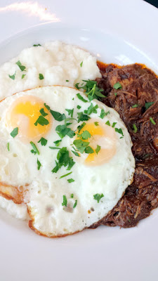 Breakfast at the Country Cat at PDX Airport of The Slow Burn with 2 sunny-side up eggs over slow cooked pork chili & grits