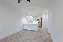 Modern apartment kitchen with white countertops, stainless steel appliances, and pendant lighting.