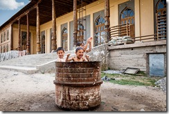 Tajik children playing in drum of water outside mosque