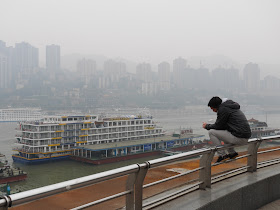 young man sitting on a railing while talking a mobile phone