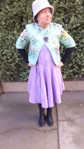 Carly findlay wearing purple dress, Aqua quilted jacket, purple hat, black boots