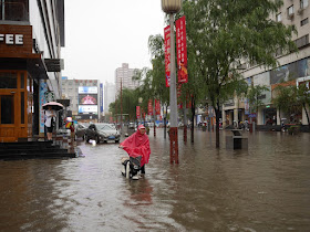 woman pushing scooter on a flooded street in Taiyuan, China