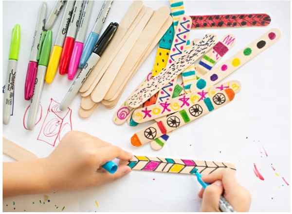 A child drawing with different colors on popsicle sticks