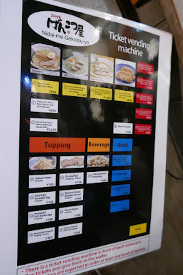 At Shin Yokohama Ramen Museum, similar to many ramen shops, at each place you order from a machine. Here luckily plastic laminated menus explain the dishes in Japanese, Chinese, Thai, and English with corresponding numbers to match the machine you will insert money and get your food ticket from.