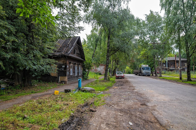 Асфальтовая улица, синяя колонка и деревянный дом