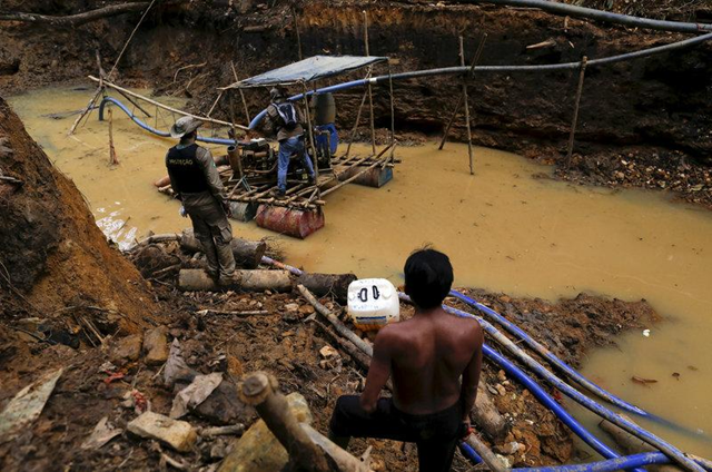 An Yanomami Indian (R) stands near an illegal gold mine during Brazil’s environmental agency operation against illegal gold mining on indigenous land, in the heart of the Amazon Rainforest, in Roraima State, Brazil, 17 April 2016. Photo: Bruno Kelly / REUTERS