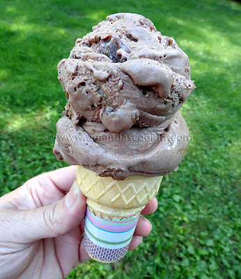 A photo of chocolate rum raisin ice cream on an ice cream cone.