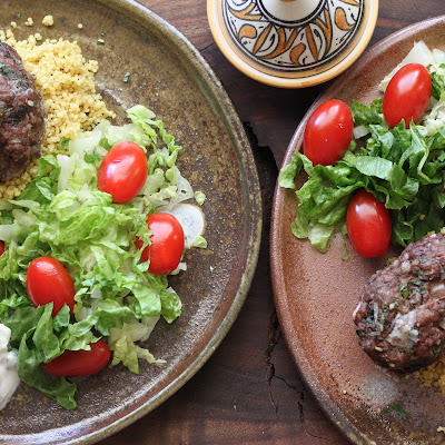 2 plates with oven baked beef kofta. Cucumber yogurt sauce, lettuce, tomato and couscous.