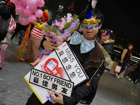 young man wearing carnival mask selling signs reading 'I miss you' and 'No.1 boy friend'