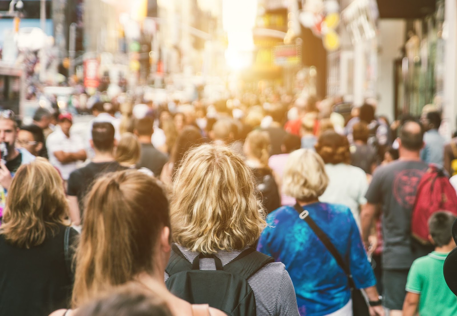 crowd of people from behind walking in a major city during sunset