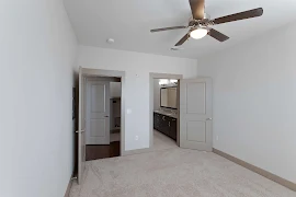 Bedroom with beige carpet, grey walls, and grey doors & molding. Bown wood ceiling fan overhead.