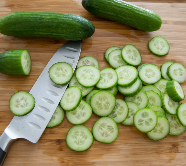 overhead photo of sliced cucumber on a cutting board with a knife