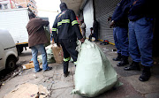 Police officers watch as workers pull bags of seized counterfeit goods. 