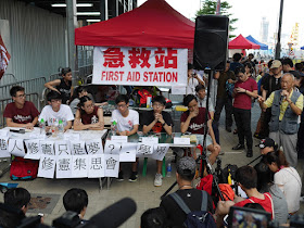 man giving a speech with Joshua Wong in attendance